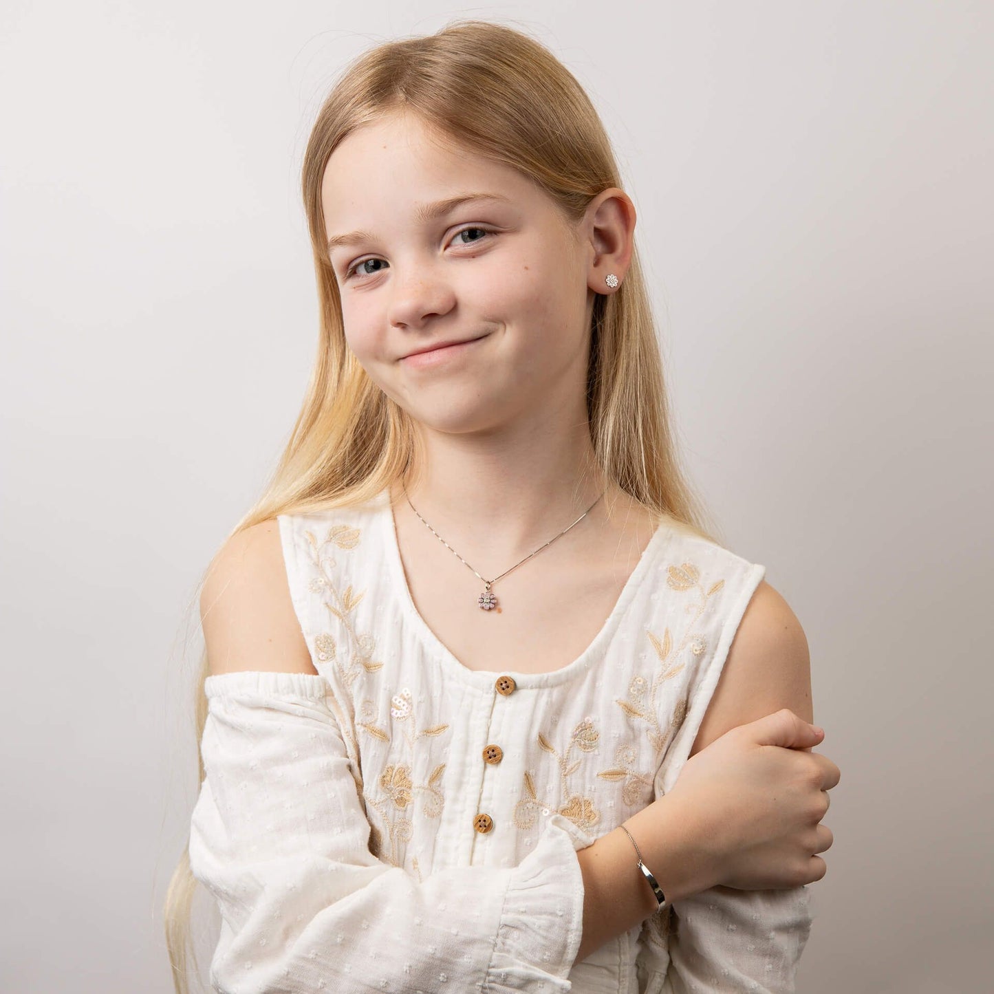 Child wearing children's silver and pink flower pendant set, featuring a delicate floral design with a matching bracelet and earrings, perfect for adding a touch of charm and elegance to a young jewelry collection.