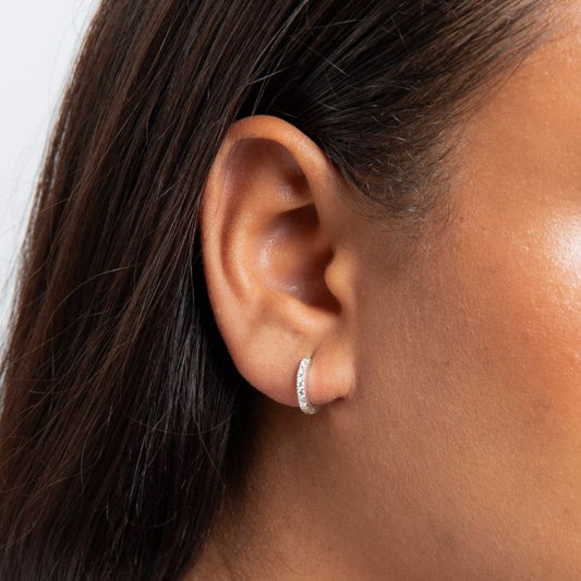 Close-up of an ear wearing a silver Crystal Hoop Earrings huggie style sleeper clasp hoops with dark hair.