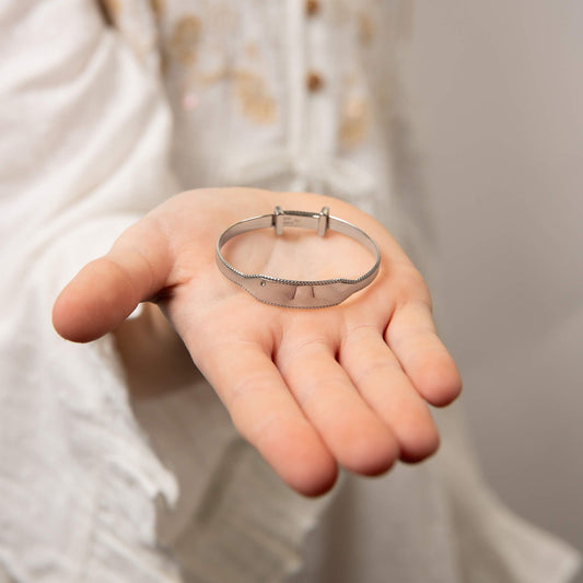 Child model holding expandable silver engravable bangle with diamond, featuring a sleek and polished design with a customizable engraving area and a sparkling diamond accent, perfect as a timeless keepsake for babies and children.