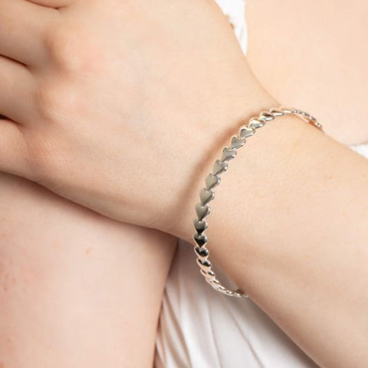 Close-up of a hand wearing a silver heart bangle 6mm bracelet on a light background