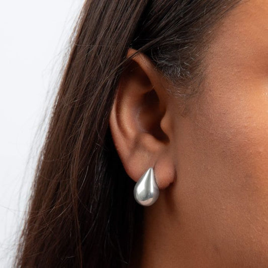 large Silver teardrop earring worn by a person with dark hair.