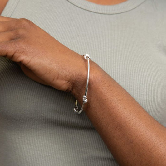 love knot bangle Silver bracelet on a wrist against a neutral background
