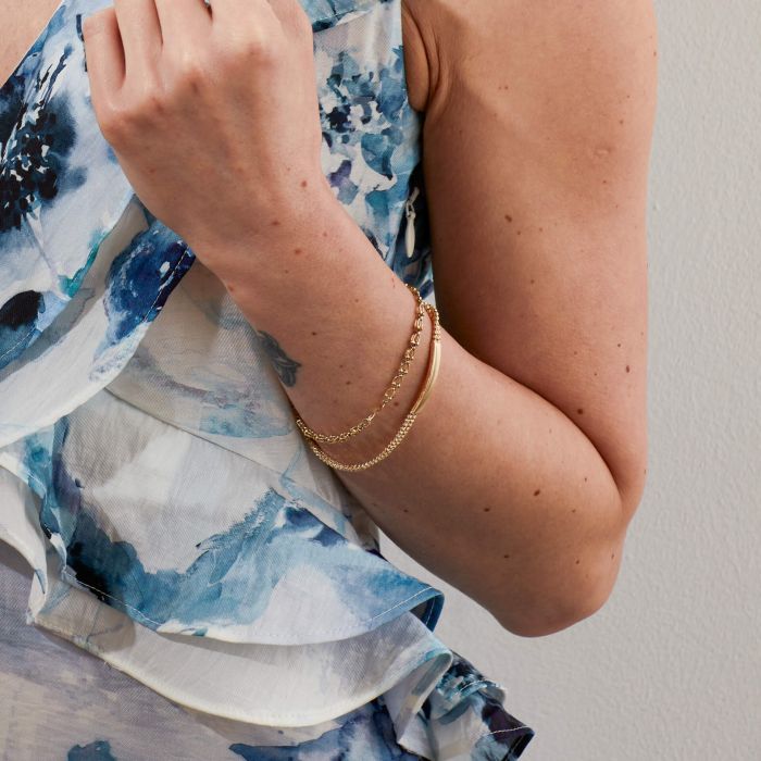 Model wearing Oval Link Bracelet in 9ct Gold stacked with Gold ID Bar Chain Bracelet, featuring interlocking oval links in polished 9ct gold and a sleek ID bar chain design, perfect for creating a layered, elegant look.