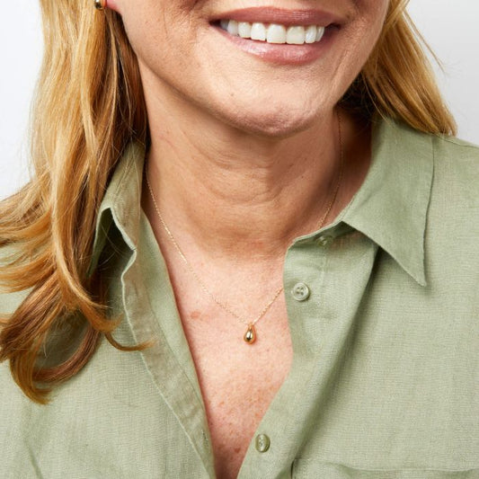 Woman wearing a green shirt with a necklace featuring a small chunky gold teardrop pendant.
