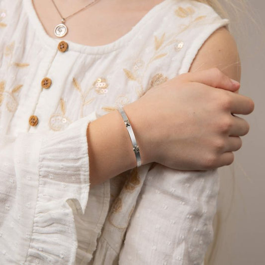 Child model holding Teddy Bear Peekaboo Expanding Bangle with Diamond b5484, featuring an adorable teddy bear design with a sparkling diamond accent on a polished silver expandable bangle, perfect as a timeless keepsake for babies and children.