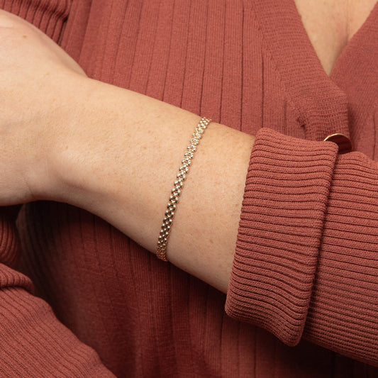 Close-up of a person arm wearing gold watch strap style bracelet on a matching rust-colored outfit.
