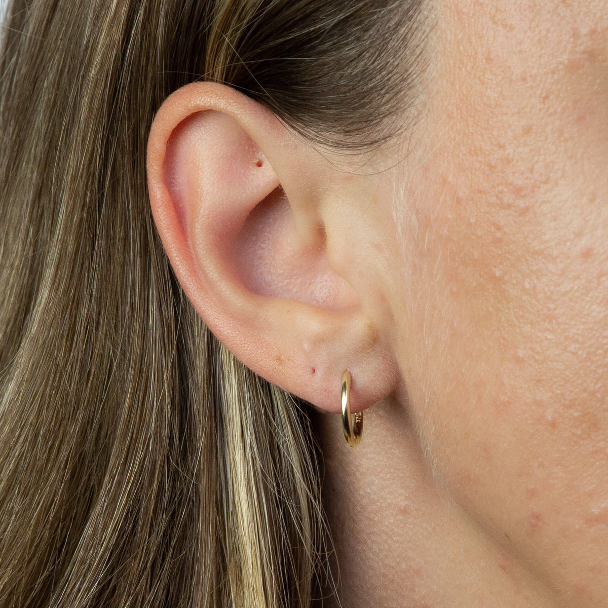 close up ear wearing gold hoop Huggie earring