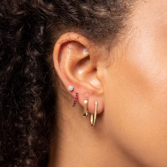 close up of ear wearing U hoop gold earrings with other earrings stacked style.