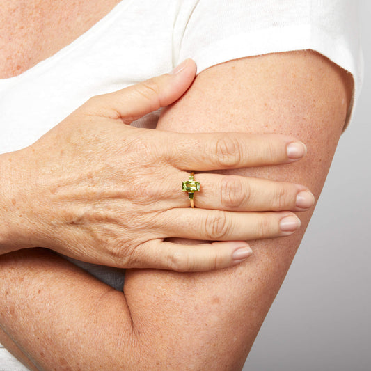 Female hand wearing Trilogy Peridot 9ct Gold ring. against a neutral light background