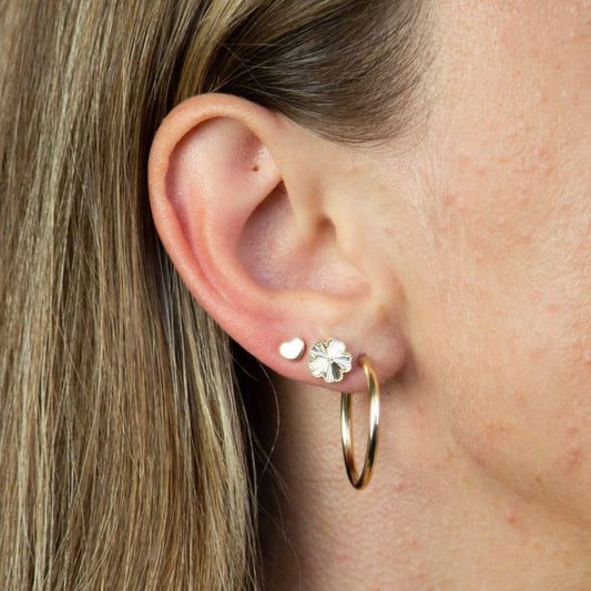 model ear wearing white gold plain heart stud earrings stacked style with two other earrings. weather worn as a stand alone earring or stacked this studs is great for simple every day wear and durable for just that.