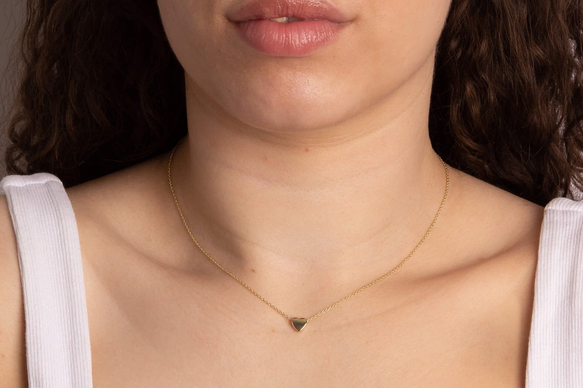 Close-up of a person wearing woman wearing Gold Small Heart necklace.