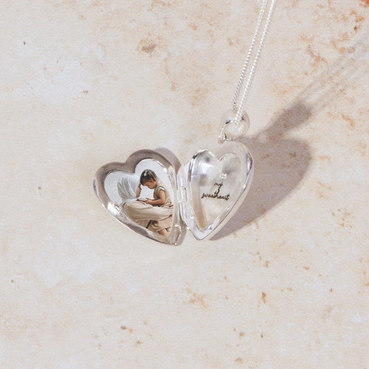 one of our bestseller at silverage london silver heart locket with image and personalised message engraving in it. open silver locket on pink marble sone background