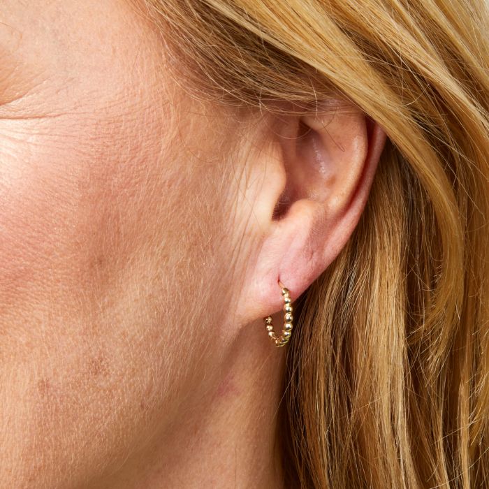 A side view of a woman wearing a pair of Ball Hoop Gold Earrings in 9ct Gold