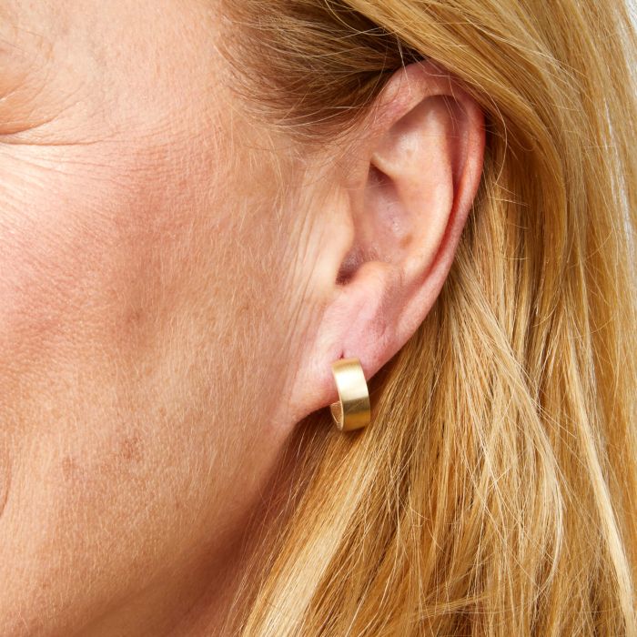 Model wearing Brushed Chunky Huggie Hoop Earrings in 9ct Gold, featuring a bold and modern brushed gold finish with a sleek huggie hoop design, perfect for adding elegance and contemporary style to any outfit.