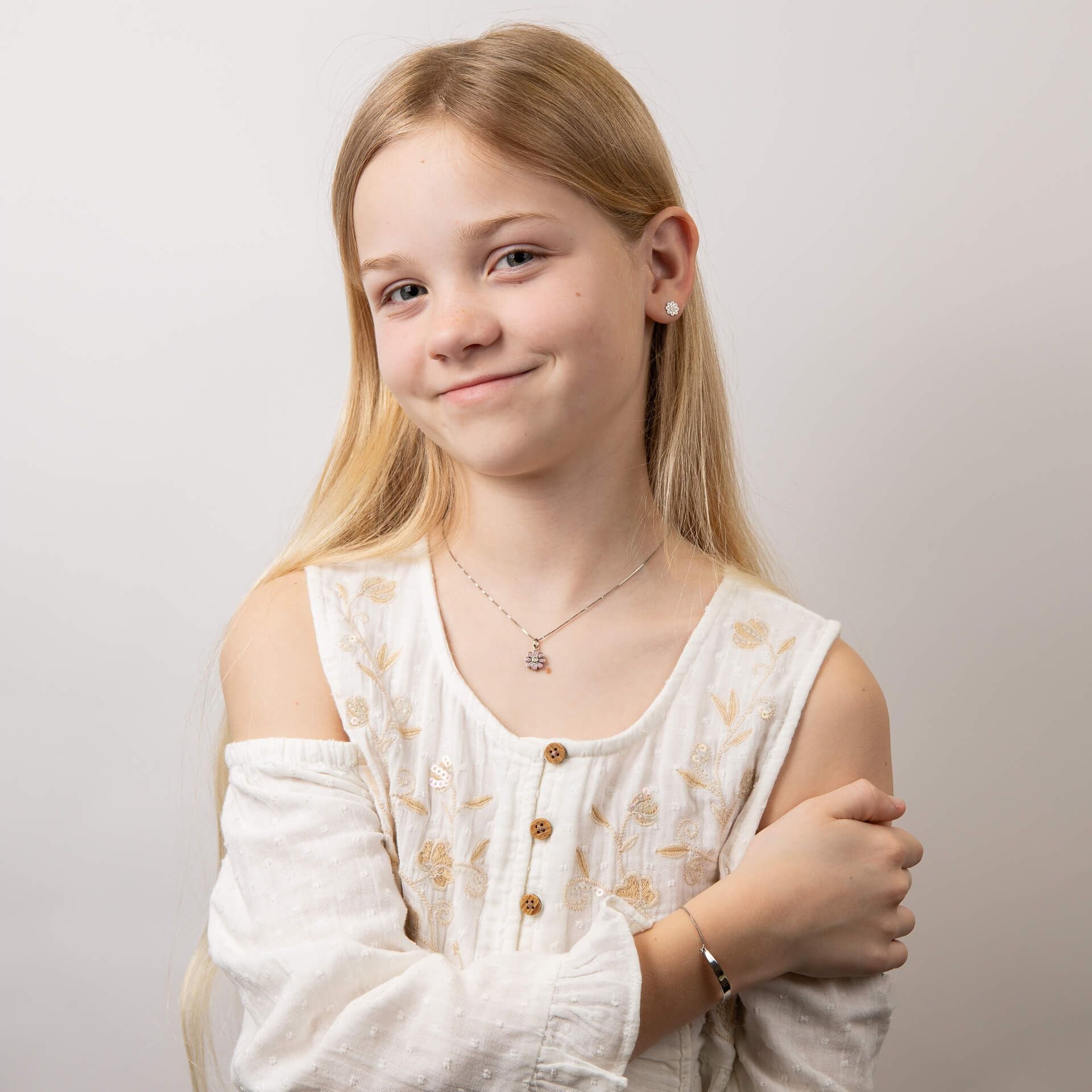 Child wearing children's silver and pink flower pendant set, featuring a delicate floral design with a matching bracelet and earrings, perfect for adding a touch of charm and elegance to a young jewelry collection.