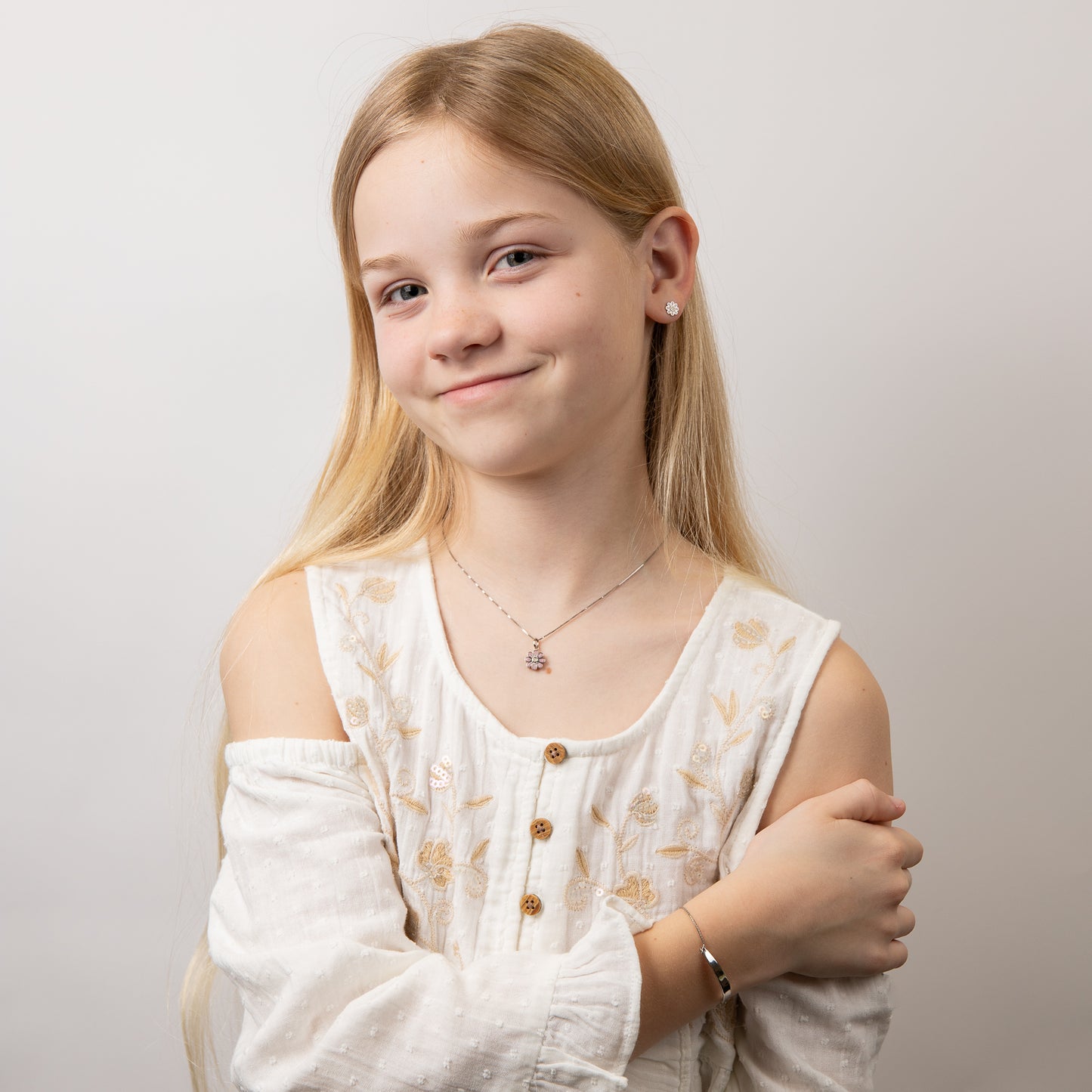 Child wearing children's silver and pink flower pendant set, featuring a delicate floral design with a matching bracelet and earrings, perfect for adding a touch of charm and elegance to a young jewelry collection.