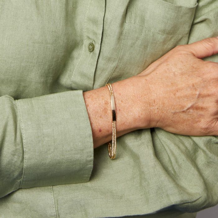 Model wearing Engravable ID Bar Double Bead Chain Bracelet in 9ct Gold, featuring a sleek double bead chain and customizable ID bar, perfect for elegant and personalized jewelry.