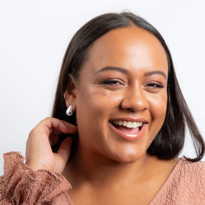 Woman with a warm smile, wearing Highly Polished Droplet Silver Stud Earrings, against a plain background how it looks on from far