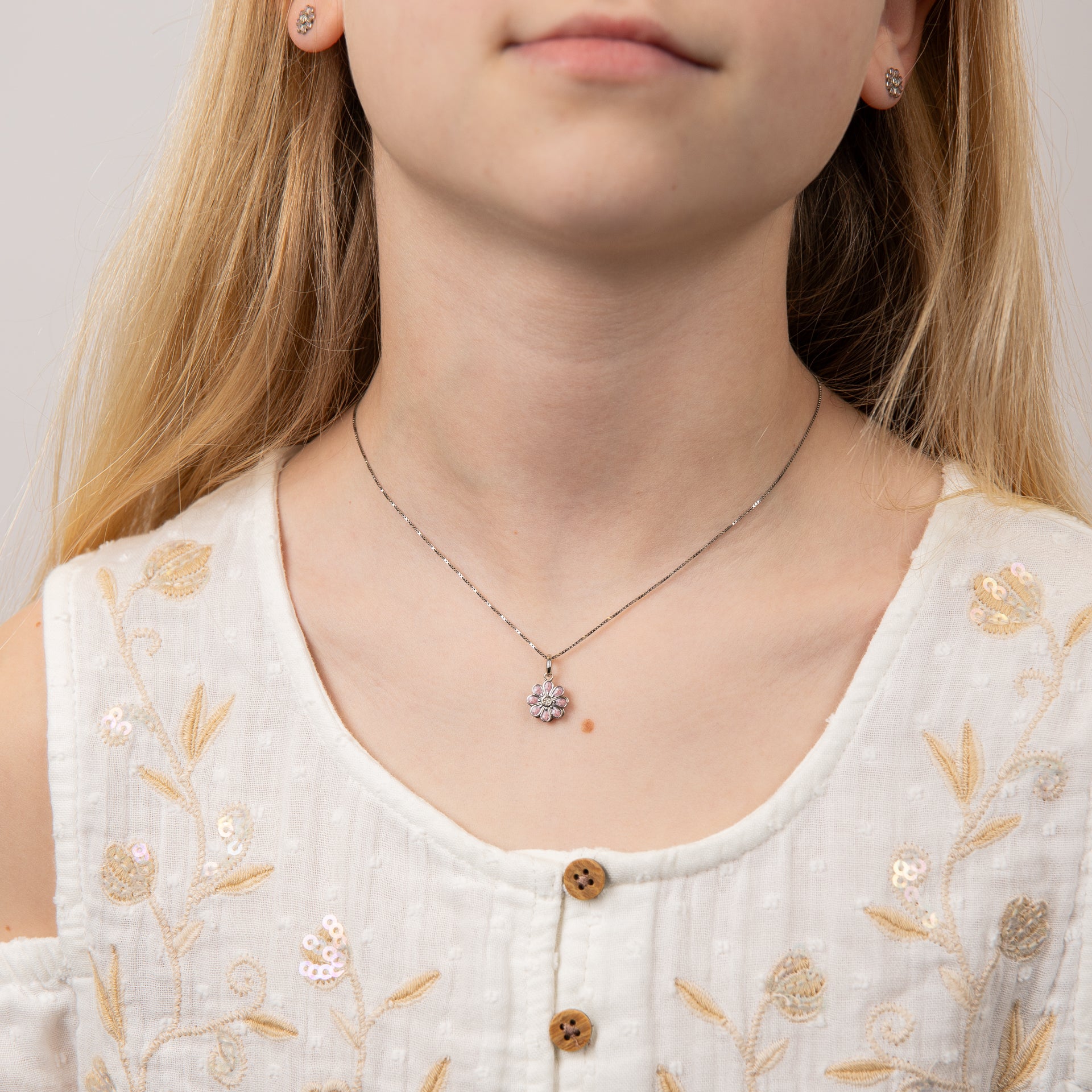 close up of Child wearing silver and pink flower pendant necklace, featuring a delicate floral design with a polished silver finish and soft pink enamel accents, perfect for adding charm and elegance to a young jewellery collection.
