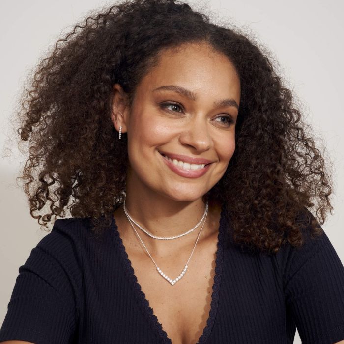 Woman with curly hair wearing a dark blue top and cubic zirconia necklace in V-shaped silver necklace layered with choker necklace white background