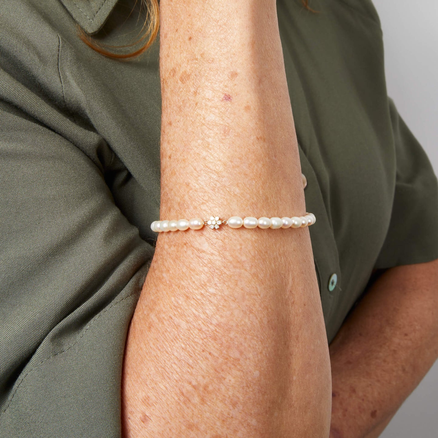 arm wearing Seed Pearl and Flower Gold bracelet against green shirt in light background 