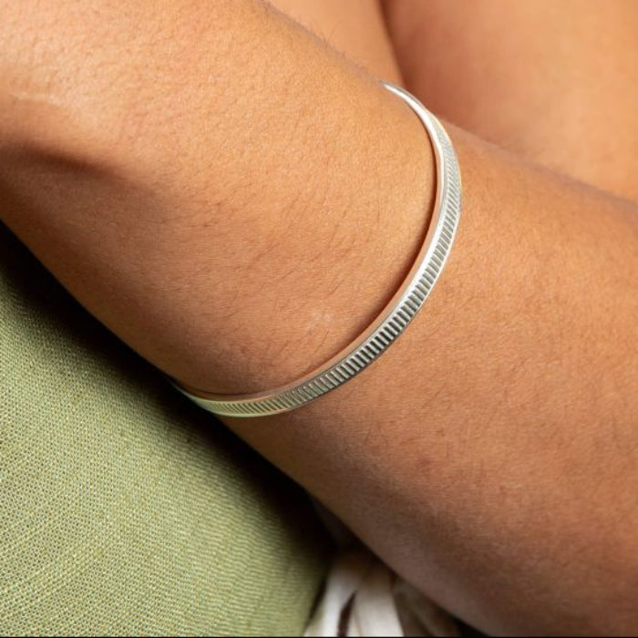 Close-up of a person's arm wearing a Ridged Spinner silver Bangle bracelet on a light background