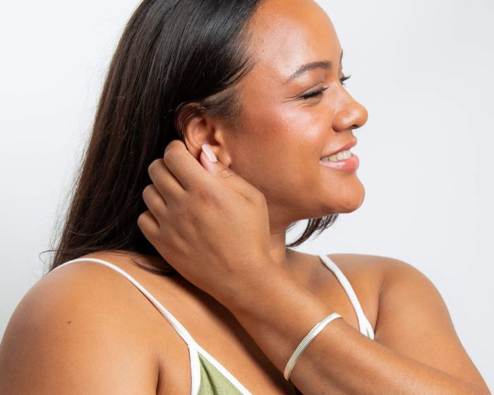 Woman adjusting an earring wearing Ridged Spinner silver Bangle against a plain background