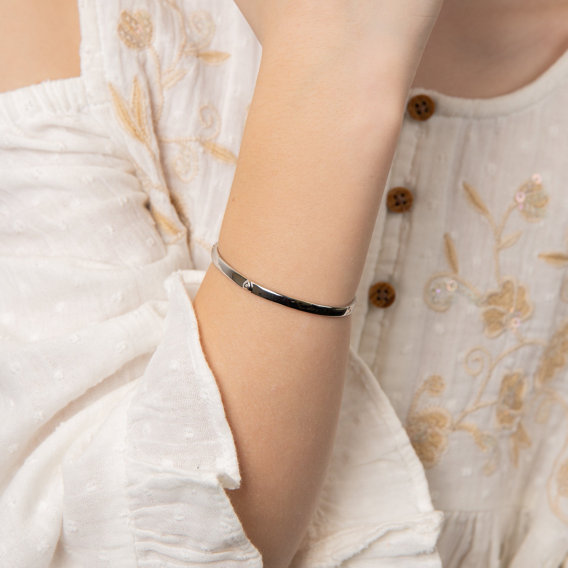 A close-up of a child wrist wearing Heart Motif Hinged Maiden Bangle bracelet, styled with a white embroidered blouse.