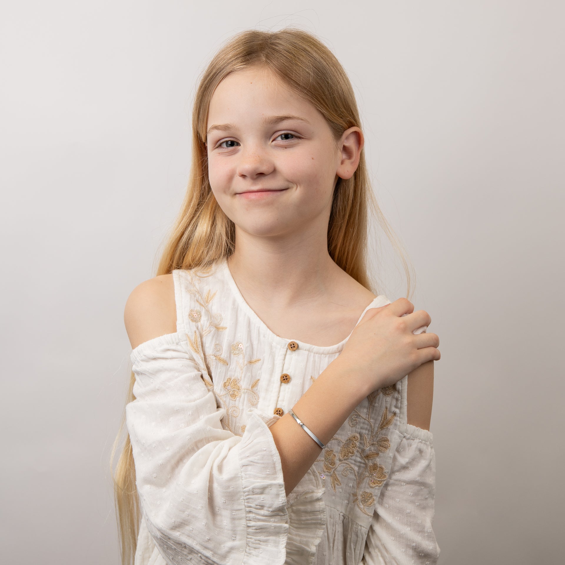A from far of a child wrist wearing Heart Motif Hinged Maiden Bangle bracelet, styled with a white embroidered blouse.