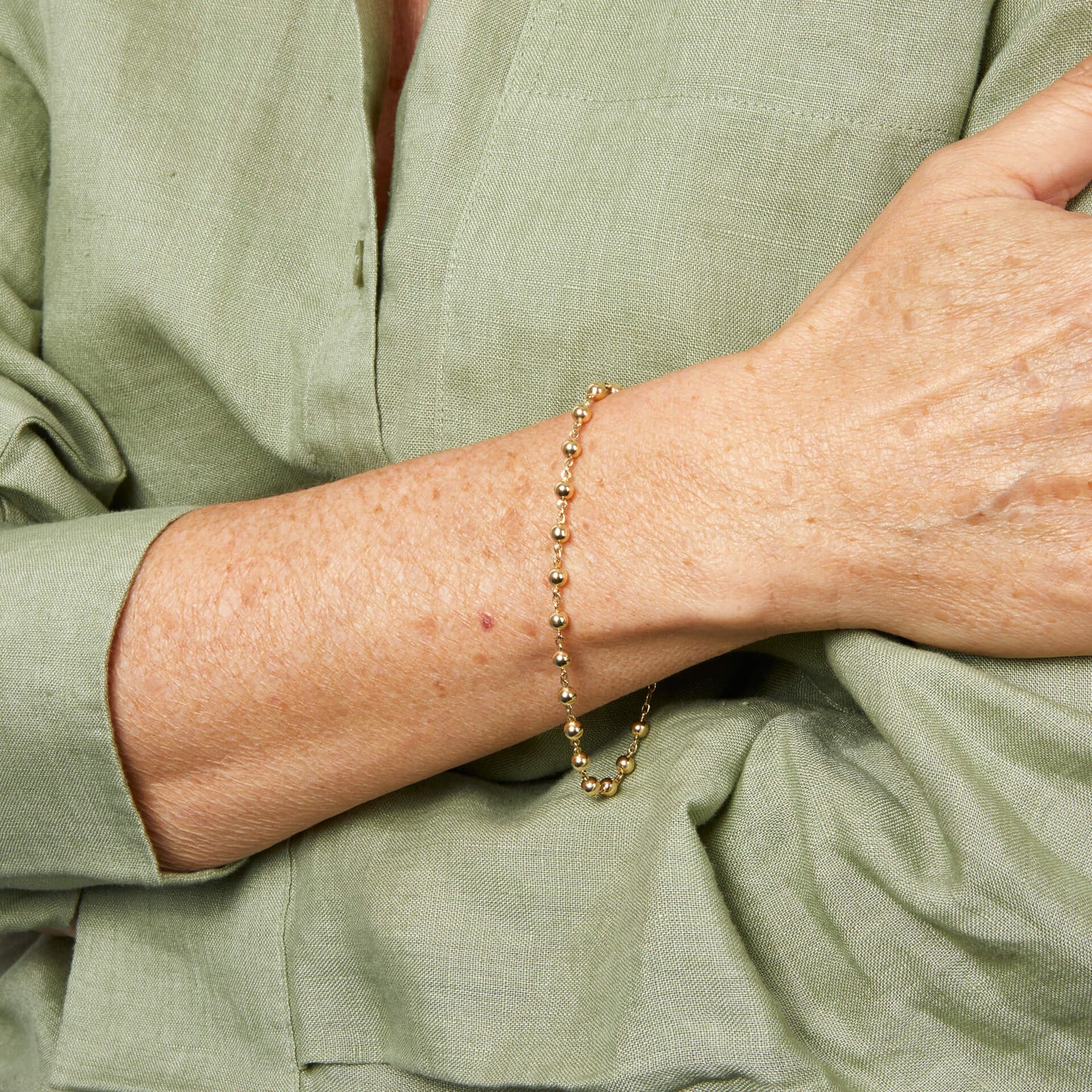 close up arm wearing Gold Ball Chain Bracelet against white shirt 