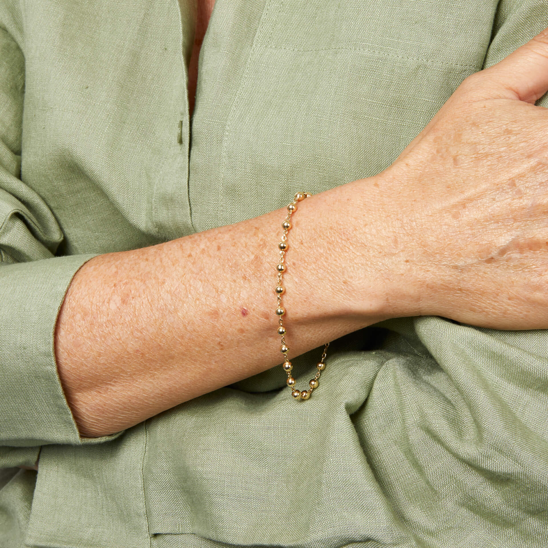 close up arm wearing Gold Ball Chain Bracelet against white shirt 