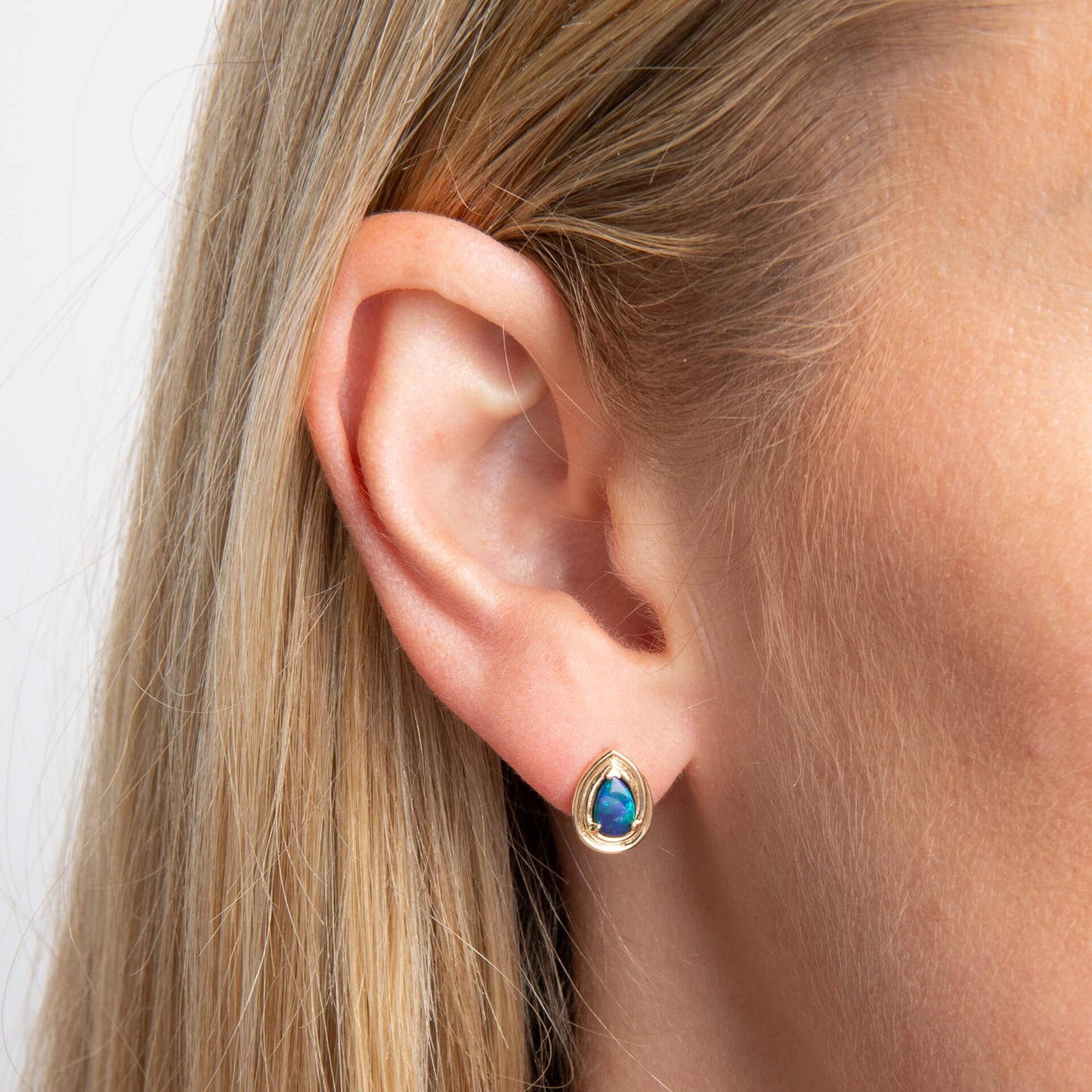 close up ear wearing 9ct Gold Australian Blue Opal Doublet Teardrop Stud Earring against white background 