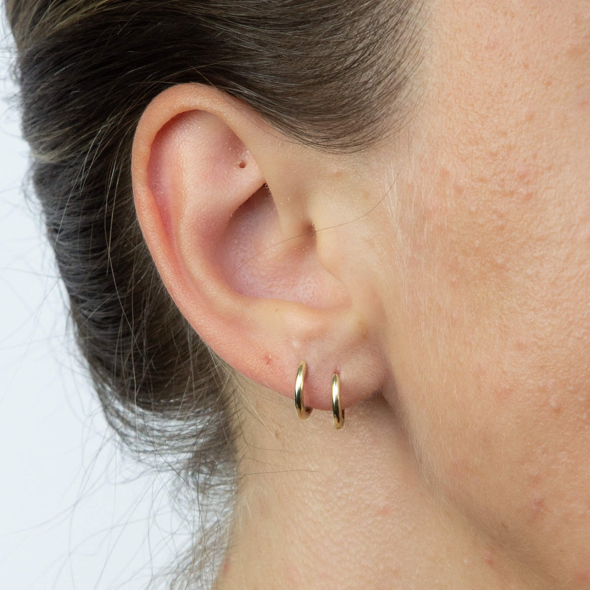 close up of ear wearing gold hoop Huggie earring stacked with another gold hoop earring gy014c_1