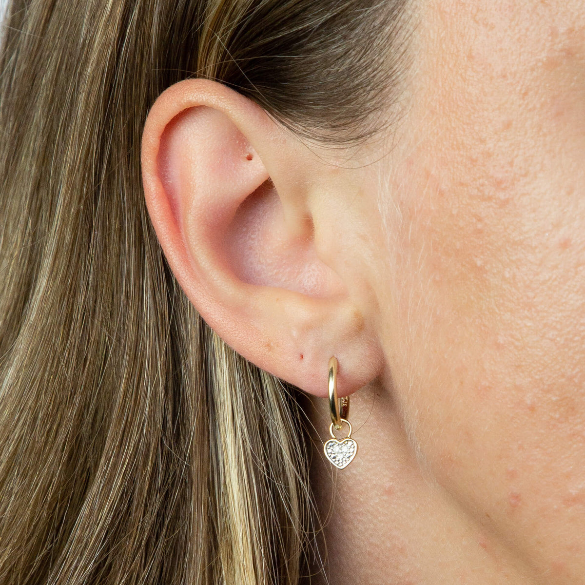 close up of ear wearing gold hoop Huggie earring with charm