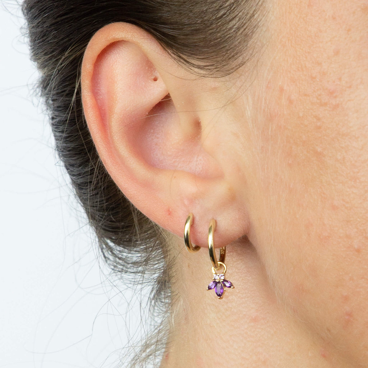 close up of ear wearing gold hoop Huggie earring with charm