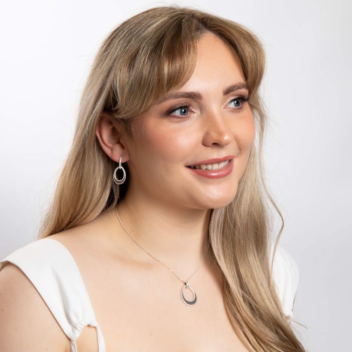 Woman wearing Open Tear drop silver Earrings with Mille grain Edge set against a plain background