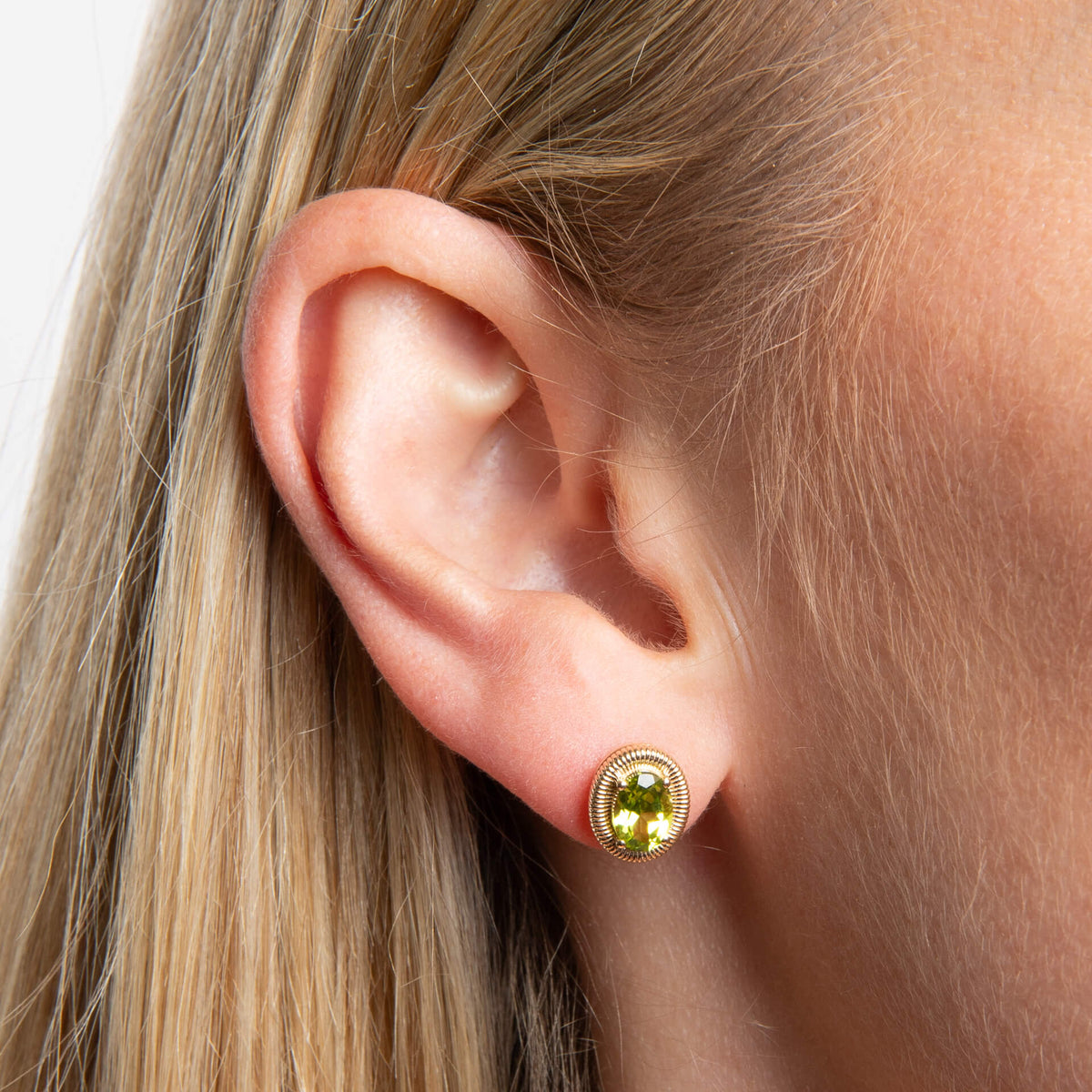 ear wearing 9ct Gold Peridot Oval Ridged Stud Earrings on white background 
