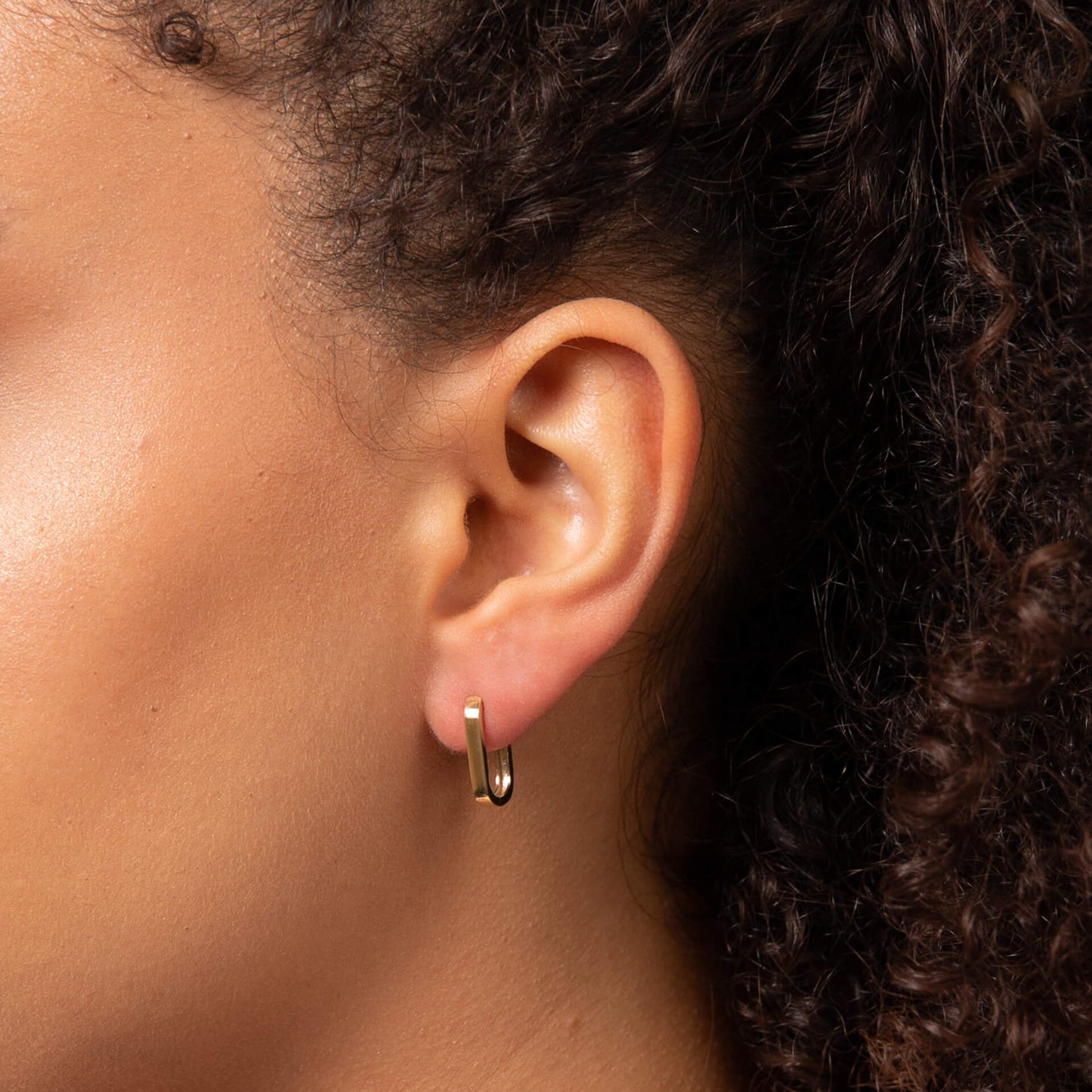 Close-up of an ear wearing Gold U hoop earring with dark hair.