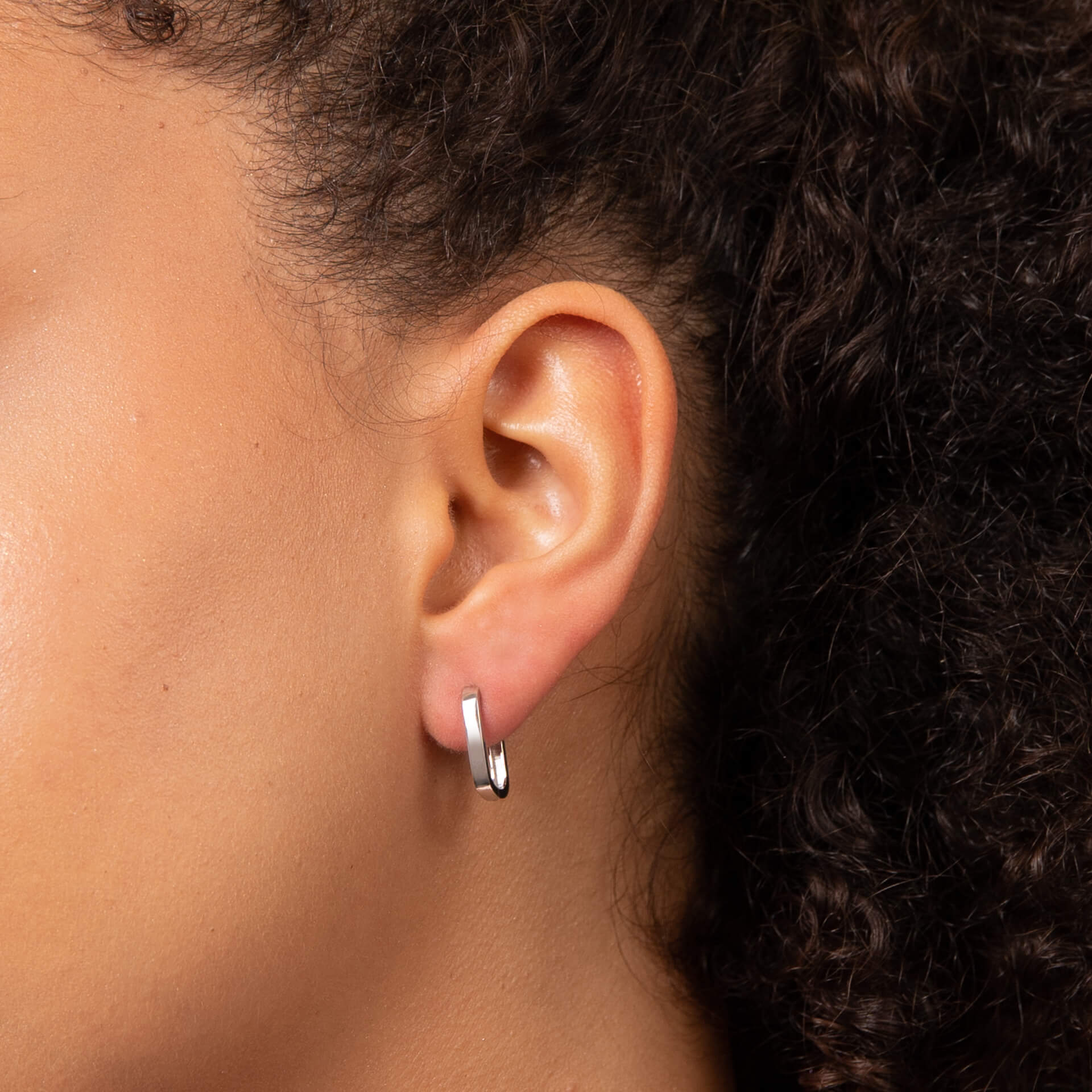 Close-up of an ear wearing a white gold U hoop earring with dark hair.