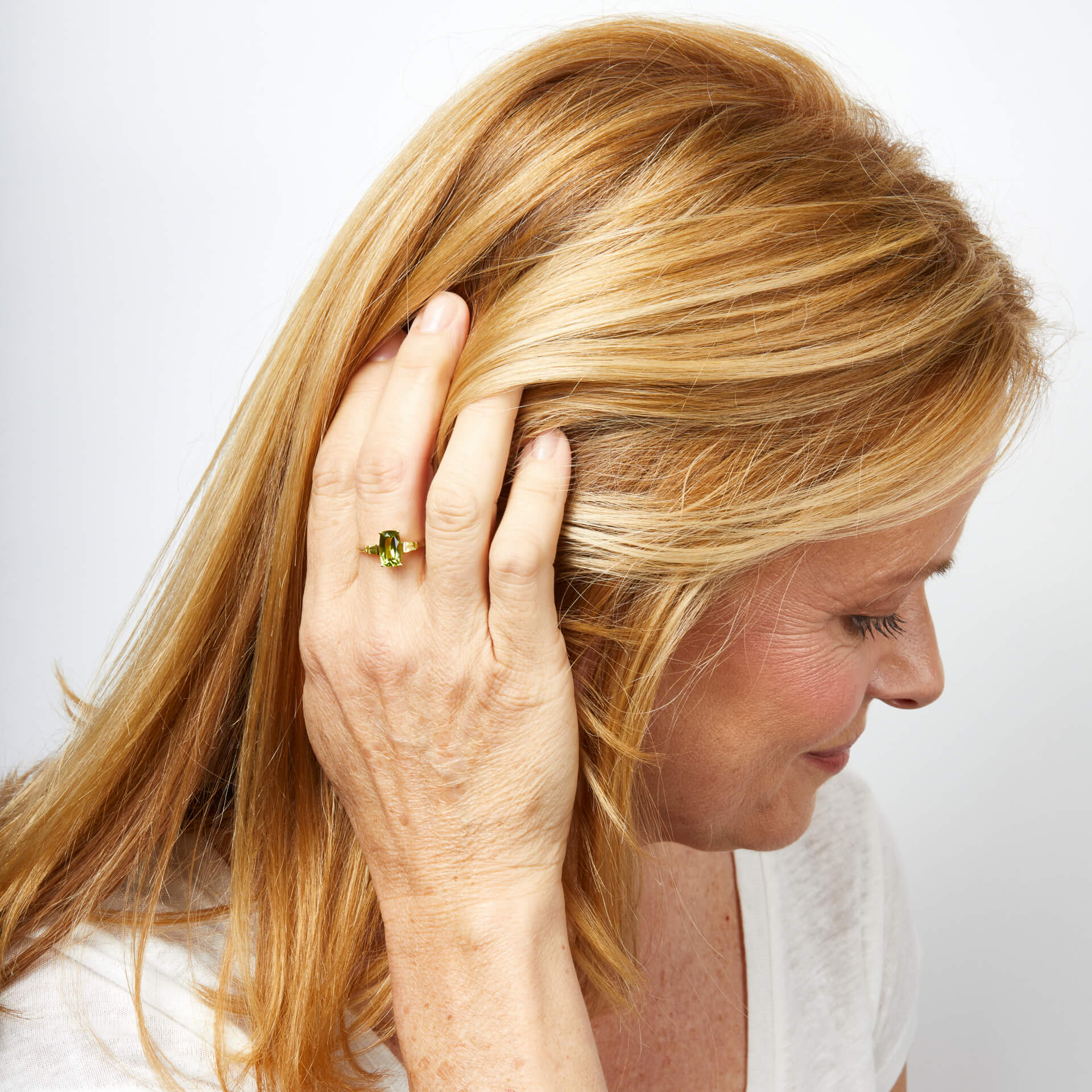 Woman with blonde hair touching her hair showing female hand wearing Trilogy Peridot 9ct Gold ring on her finger. against a white background