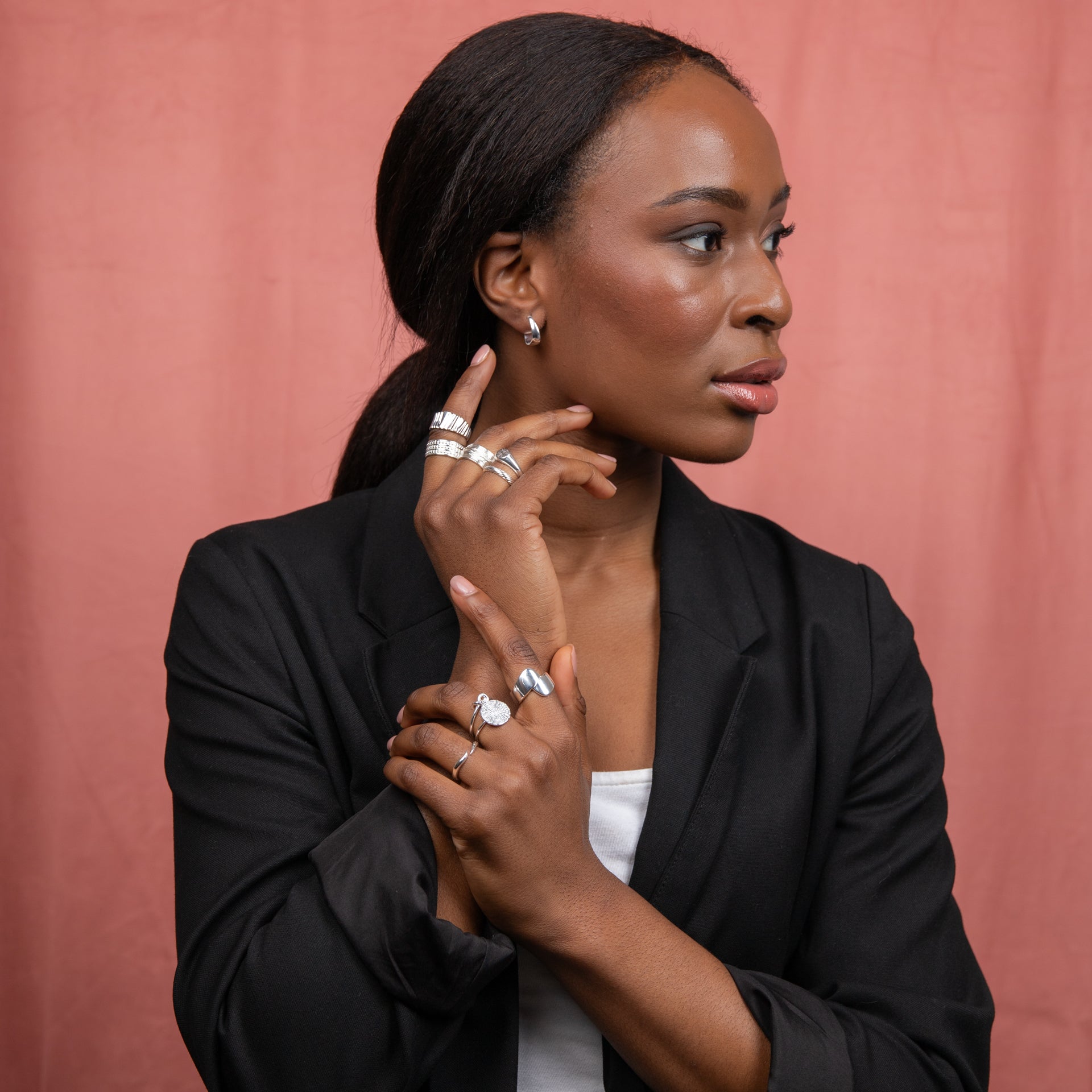 model wearing love knot ring and other silver jewellery stacked on hand showcasing how to style sophisticated look outfit black blazer and white shirt model against a plain peach background