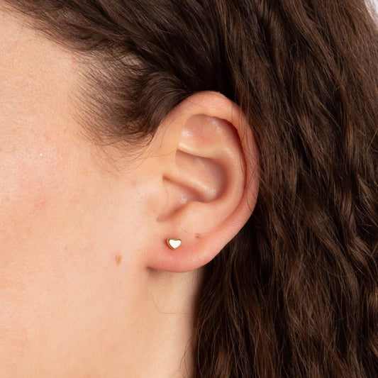 model ear wearing gold plain heart stud earrings alone. weather worn as a stand alone earring or stacked this studs is great for simple every day wear and durable for just that.