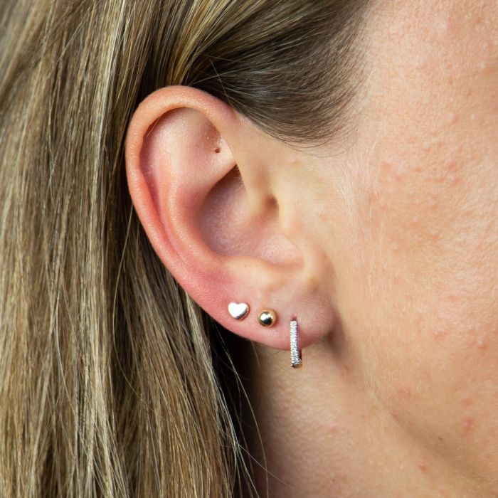 model ear wearing white gold plain heart stud earrings stacked style with  two other earrings. weather worn as a stand alone earring or stacked this studs is great for simple every day wear and durable for just that.