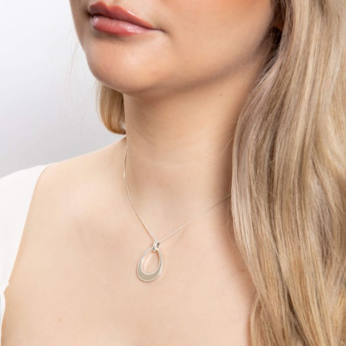 Woman wearing a Open Tear drop silver Pendant with Mille grain Edge necklace on a plain background