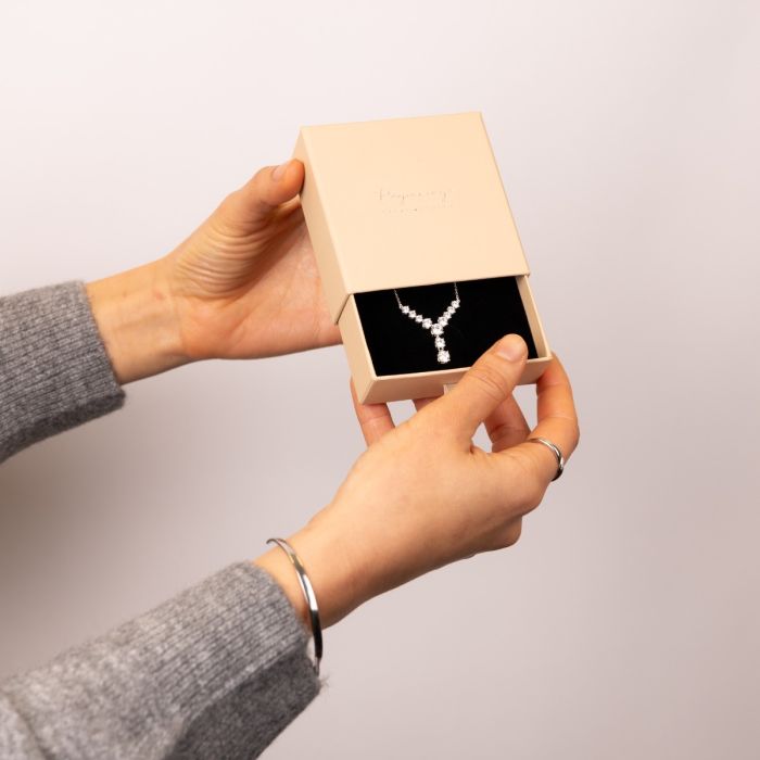 Person holding a jewellery box crafted from premium recycled materials. with a necklace inside against a plain background