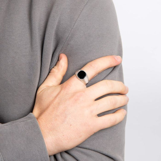Person wearing a gray sweater with a hand wearing a black onyx silver ring with ripple detail against their chest.