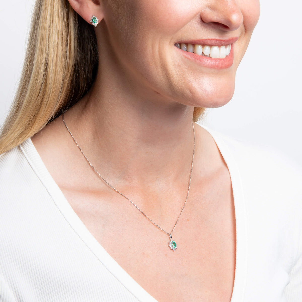 woman wearing 9ct White Gold Emerald Art Deco Pendant necklace and earrings set on white background with white top