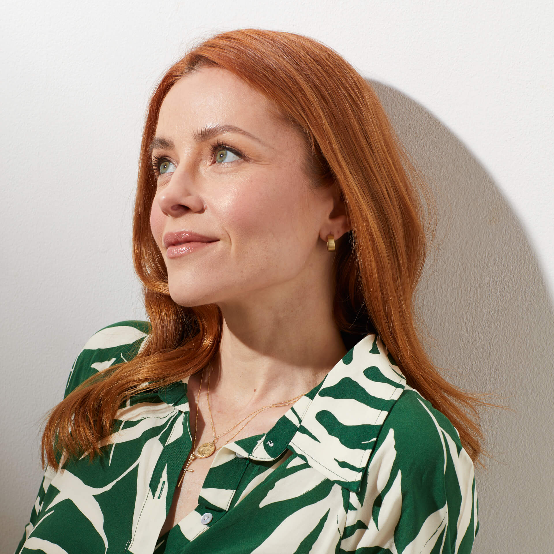 woman from far view wearing Brushed Chunky Gold Hoop Earrings with layered gold necklaces with green and white floral shirt. 