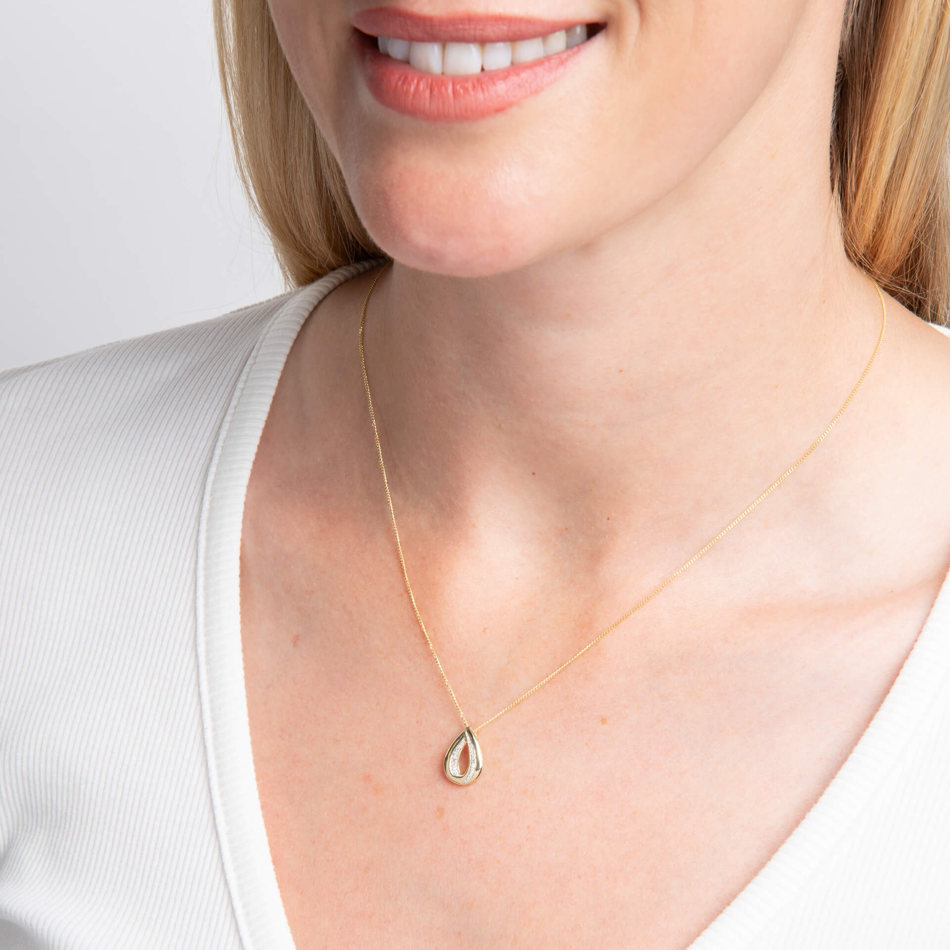 woman wearing Gold Cut Out Diamond Teardrop Pendant necklace with white top on white background