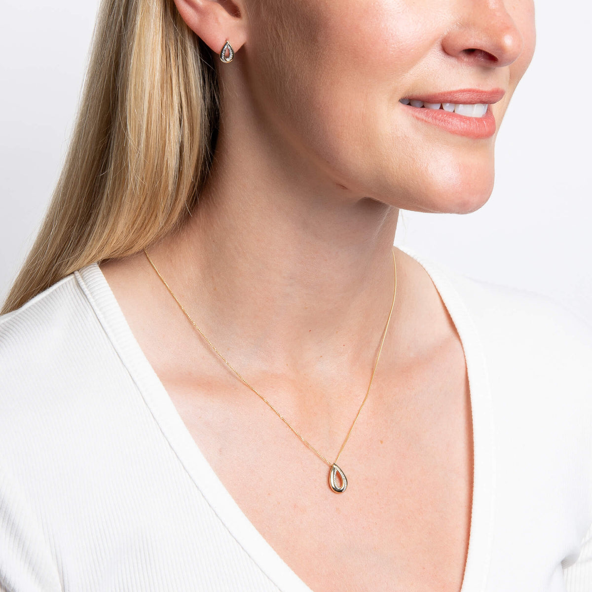 woman wearing Gold Cut Out Diamond Teardrop Pendant necklace and earrings with white v neck top on white background 